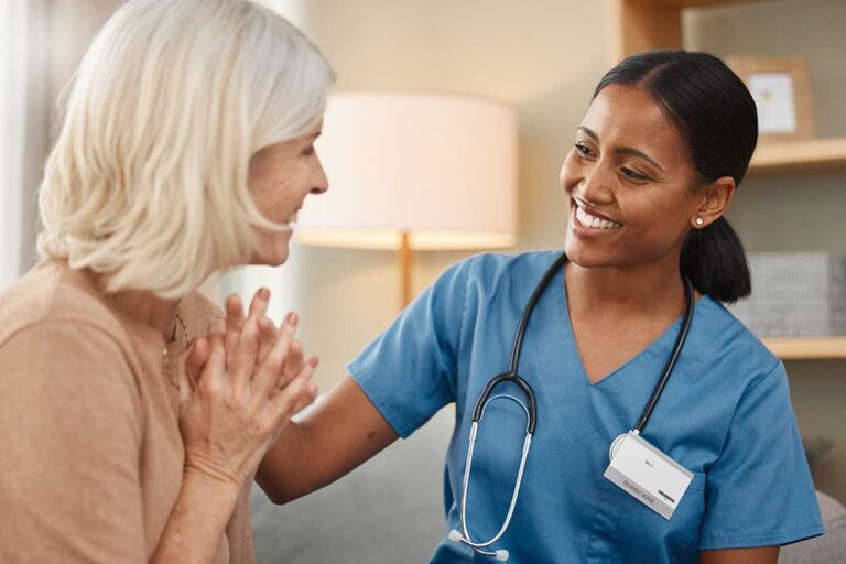 A social worker speaks with an older adult at a small table in a bright, comfortable community room.